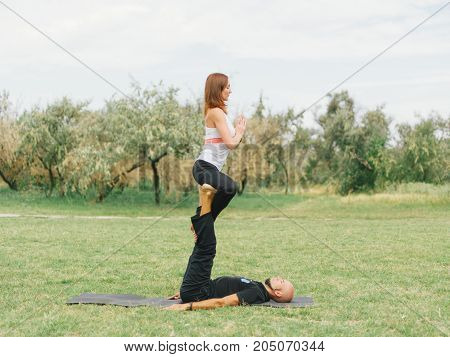 Beautiful woman and man practise yoga pose outside. Women doing stretching workout in park outdoors at sunset.