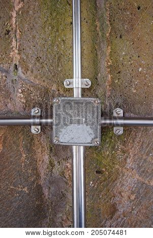 outdoor electrical junction box in metal with conduits and fixtures fastened to a stone wall