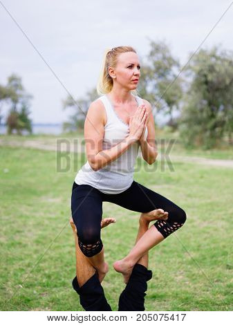 Girl in white shirt exercises yoga outdoor, on green grass.