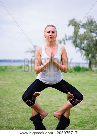 Girl in white shirt exercises yoga outdoor, on green grass.