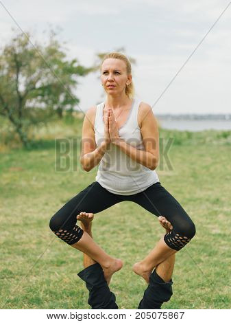 Girl in white shirt exercises yoga outdoor, on green grass.