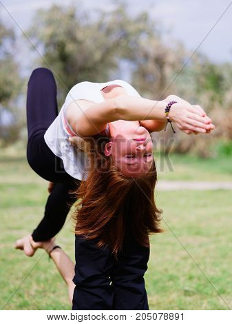 Girl in white shirt exercises yoga outdoor, on green grass.