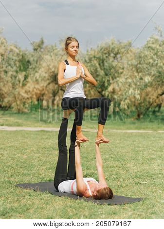 Girl in white shirt exercises yoga outdoor, on green grass. Blue sky on the background.