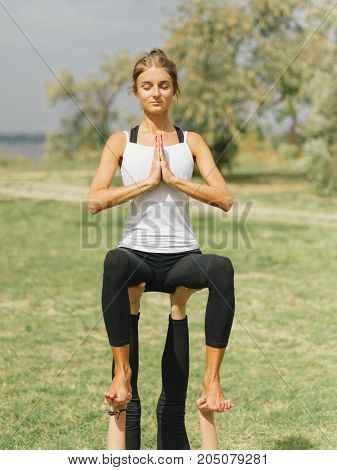 Girl in white shirt exercises yoga outdoor, on green grass.