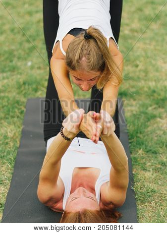 Girl in white shirt exercises yoga outdoor, on green grass. Blue sky on the background.