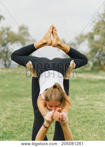 Girl in white shirt exercises yoga outdoor, on green grass. Blue sky on the background.