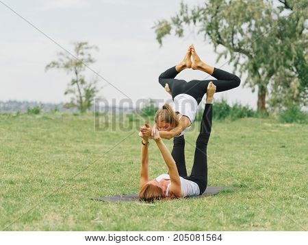 Girl in white shirt exercises yoga outdoor, on green grass. Blue sky on the background.
