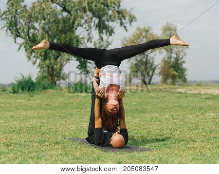 Women doing stretching workout in park outdoors at sunset. Beautiful woman and man practise yoga pose outside.