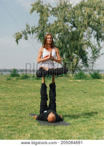 Women doing stretching workout in park outdoors at sunset. Beautiful woman and man practise yoga pose outside.