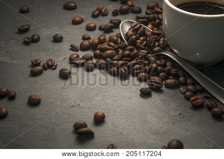 A coffee cup with a spoon and some coffee beans on a gray background