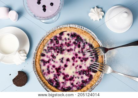 Homemade open pie with blueberries and cream filling served with marshmellows and milk on pale blue background above view