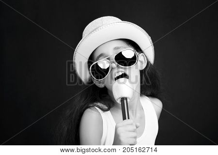 Little girl rocker with sunglasses microphone and hat on a black background