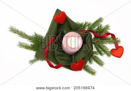 Christmas present bag with red ribbon bow with candle and red heart shape toy laying in fir tree branches isolated on white background. Christmas decoration.