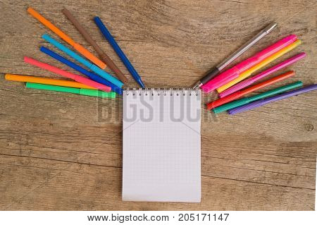 Open white notepad with colorful felt-tip pens and ball pens on the wooden table