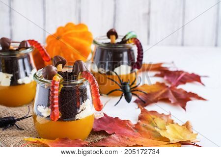 Layered halloween dessert with pumpkin jello, cream and chocolate cookies in glass jars on autumn background. Selective foucs