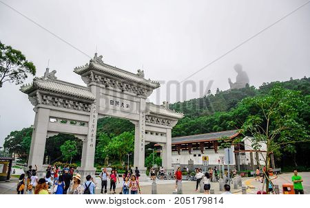 HONG KONG - MAY 31: Tourists at the gate to Po Lin Monastery with Tian Tan Buddha statue up on the hill in background, Ngong Ping Village, Lantau Island, Hong Kong