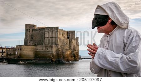 Pulcinella traditional Neapolitan mask gestures with Castel dell'Ovo in the background in the Gulf of Naples.