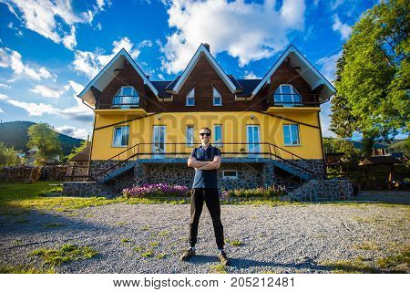 Happy young businessman in sunglasses bought a big home. Man standing with thumbs up near his new home