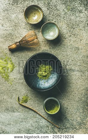Flat-lay of Japanese tools for brewing matcha tea. Matcha powder in tin can, Chashaku spoon, Chasen bamboo whisk, Chawan bowl and ceremony cups over concrete background, top view, vertical composition
