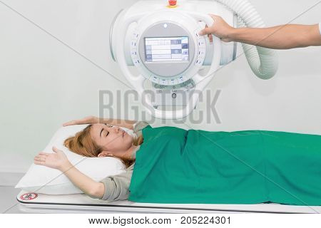 Asian young woman patient lying under X-ray device with radiologist preparing machine in X-ray room at hospital.