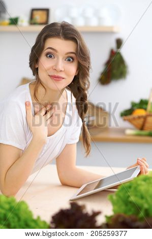 Young  woman looking for a new recipe for  cooking in a kitchen. Housewife is making online shopping by tablet computer and credit card.