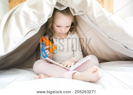 A Little girl reading fairy tales book under the covers at the evening with lantern.