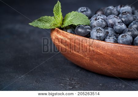 Fresh blueberries with a leaf of mint in the heart-shaped bowl on a dark blue background