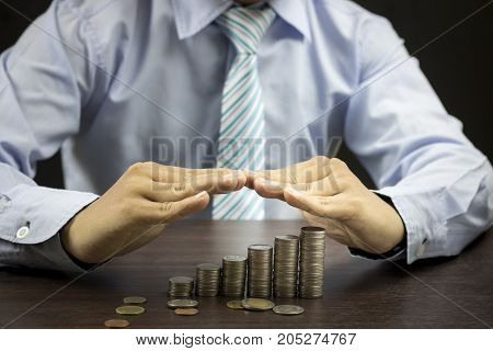 Businesman protect staced of money coins on wood table with blackbackground