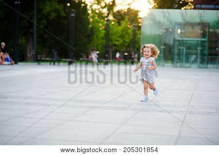 Cute little girl runs around the square in a city park. Warm summer day. Baby is very fun.