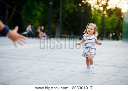 Adorable little girl runs towards the parent hands. Warm summer day. Baby is very fun.