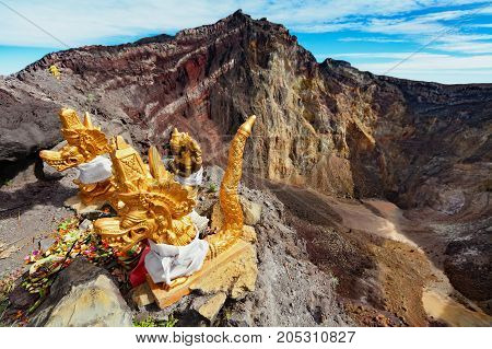 Balinese hindu shrine on brink of volcanic crater with traditional religious offering for volcano spirits protecting against eruption. Summit of active volcano Mount Agung on Bali island Indonesia.