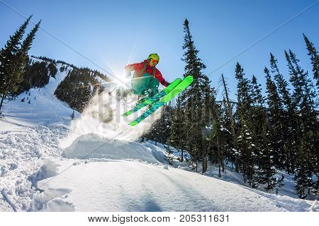 Skier Freerider Jumping From A Snow Ramp In The Sun On A Background Of Forest And Mountains