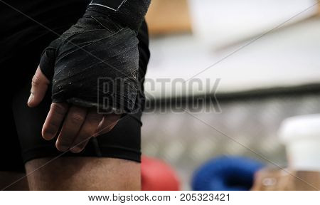 hand of the boxer before the fight bandaged with a protective bandage black bandage foreshortening on the arm against the background of the training hall with lying boxing gloves martial arts