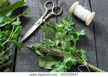 Bouquet garni. Classical french composition. Bay leaf parsley and thyme bound with culinary thread. Bunch of fresh aromatic herbs coil with threads scissors on dark wooden table
