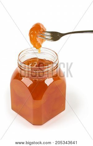 Glass jar with apricot jam. One hulf of apricot on the fork.