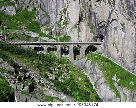 Scenic stony rail bridge in swiss Alps in SWITZERLAND near Andermatt town with alpine rocky scenery in 2017 warm summer day, Europe on July.