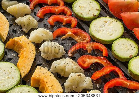 Variety of fresh vegetables prepared for cooking on grill pan. Vegetables are cut into pieces sprinkled with salt and spices laid in rows. Prepare diet vegetarian dishes. Healthy food concept