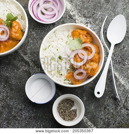 Homemade dinner butter chicken on cream with spices, cream served with basmati rice in ceramic bowls with cilantro and sweet red onion. Top View