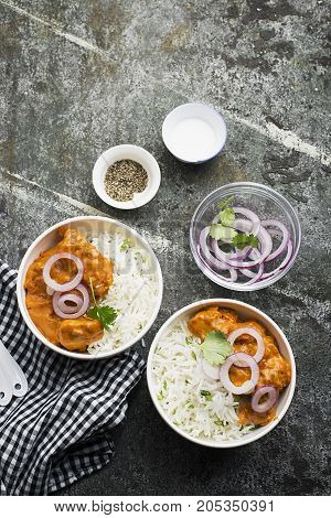 Homemade dinner butter chicken on cream with spices, cream served with basmati rice in ceramic bowls with cilantro and sweet red onion. Top View