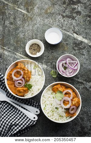 Homemade dinner butter chicken on cream with spices, cream served with basmati rice in ceramic bowls with cilantro and sweet red onion. Top View
