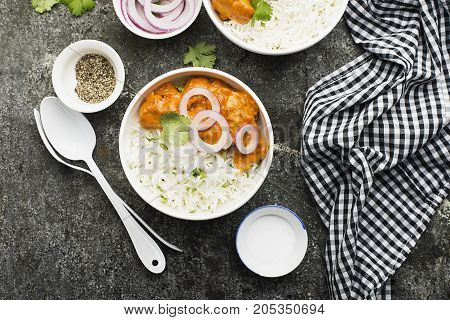 Homemade dinner butter chicken on cream with spices, cream served with basmati rice in ceramic bowls with cilantro and sweet red onion. Top View