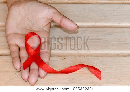 The symbolic conception of the world day of fight against AIDS. The red ribbon in the hands of a woman on wooden background.