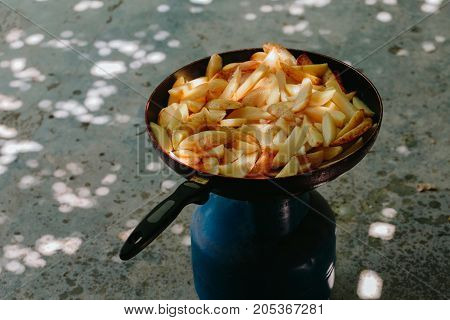 Fried potatoes in a frying pan in the yard on a gas burner