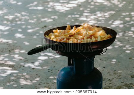 Fried potatoes in a frying pan in the yard on a gas burner