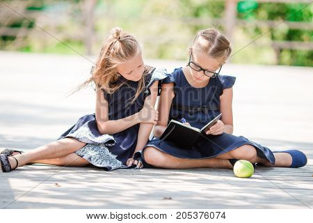Adorable little school girls with notes and pencils outdoor.