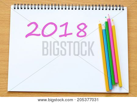 2018 on notebook paper and colorpencils on wood table background new year banner concept