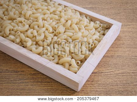 Food and Cuisine Uncooked and Dried Elbow Macaroni or Gomiti Pasta in A Wooden Tray.