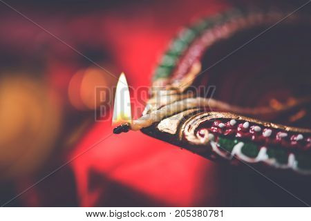 stock photo showing Diwali still life with Diya or oil Lamp, gift boxes, sweets and fire crackers with flowers arranged over red satin cloth with bokeh