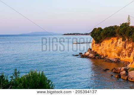 Orange sunlight is over rocky cliff at coastline.