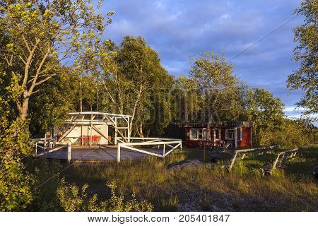 Outdoor, old wooden dance floor in the countryside. Seats and some red cabin, for sales.